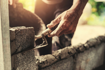 hand of worker plastering cement on brick wall at construction site