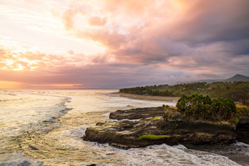 Fototapeta na wymiar Dramatic aerial sunset over a black sand coastline with rocks in Bali, Indonesia