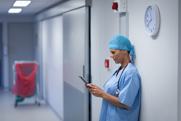 Female surgeon using mobile phone in hospital corridor