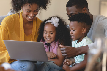 Happy African American parents with their cute children using laptop on sofa
