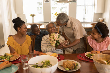 Senior man giving flower bouquet to senior woman while having meal on dining table