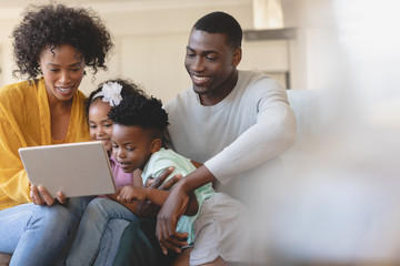 Happy African American parents with their cute children using digital tablet on sofa