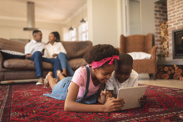 African American children lying on floor and using digital tablet while parents sitting on the sofa