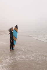 Senior female surfer with surfboard standing on the beach