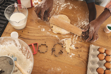 African American father and son rolling dough with rolling pin in kitchen