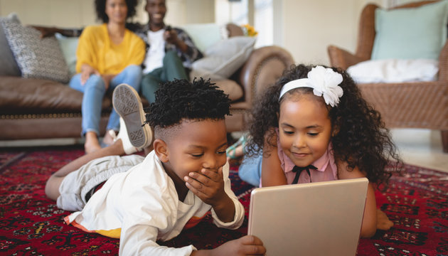 Cute African American sibling lying on floor and using digital tablet - Powered by Adobe