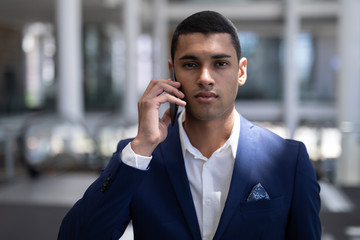 Youmg mixed-race businessman looking at camera while using mobile phone in modern office