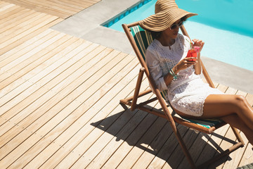 African American woman with cocktail glass relaxing on sun lounger in backyard