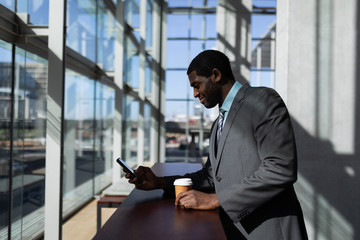 Fototapeta na wymiar African-American businessman with coffee cup using mobile phone in office