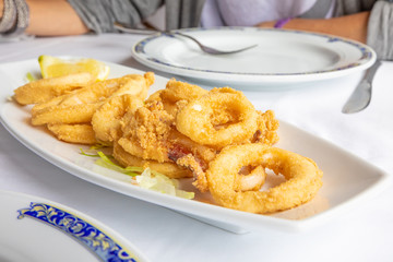 close up white tray with rings of squid, breaded and fried, with lemon and lettuce, typical food of Andalusia (Spain, Europe) on white tablecloth of restaurant ready to eat
