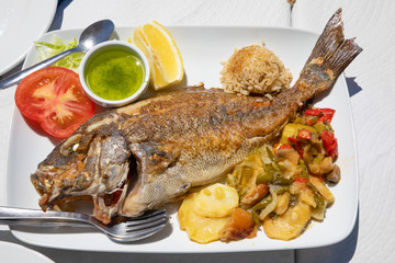 tray with a grilled fish known as Donkey or Borriquete (Plectorhinchus mediterraneus) in Spain, with potatoes and vegetables, rice, lemon and tomato