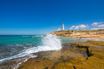 beautiful landscape: ocean wave breaking on coast rock next to lighthouse of Trafalgar Cape, near...