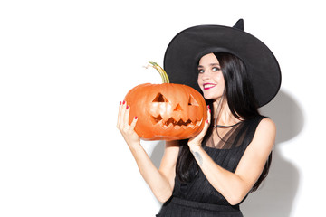 Young brunette woman in black hat and costume on white background. Attractive caucasian female model. Halloween, black friday, cyber monday, sales, autumn concept. Holding pumpkin. Look mystic.