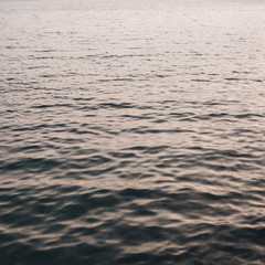 Sea or ocean water with little relaxing waves and reflection in different light. Beautiful gradient with creamy pink and dark blue colors. Neutral background and texture.