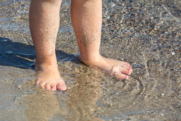 Fototapeta na wymiar Feet of small child standing in the clear ocean water at the beach