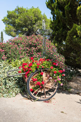 Fototapeta na wymiar Large metal decorative crossand and a wheelbarrow with flowers in the courtyard of the Greek Orthodox Monastery of the Transfiguration located on Mount Tavor near Nazareth in Israel