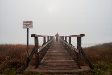 Fototapeta premium Steg im Nebel mit Mann in roter Jacke und Cap