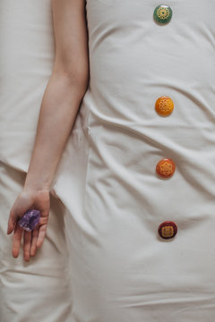 From above photo of unrecognisable cropped woman lying on massage table with chakra crystals on her body.