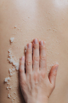 Hand of unrecognisable woman masseuse applying skin scrub on client's back.