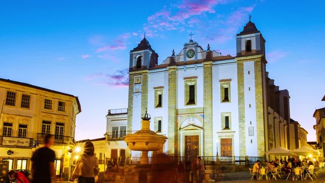 Evora, Portugal. View of Roman Catholic Cathedral of Evora, Portugal at sunset. Illuminated historical buildings at the square with motion blurred people. Time-lapse of sky gettind dark, panning video