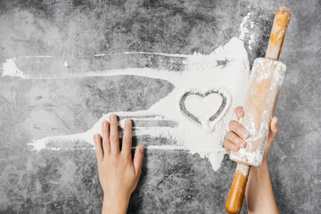 Baking background. Heart of flour, rolling pin and female hands on gray table. Bake menu, recipe, homemade pastry concept. Top view. Banner with copy space for your text. Valentine's Day