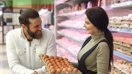Young happy couple choose eggs in supermarket. Young family buying eggs at the grocery store. Slow motion. Portrait.