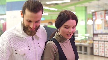 Beautiful young couple is choosing products and smiling while doing shopping at the supermarket. Couple is choosing frozen seafood for dinner in the supermarket.