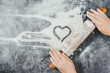 Baking background. Heart of flour, rolling pin and female hands on gray table. Bake menu, recipe, homemade pastry concept. Top view. Banner with copy space for your text. Valentine's Day