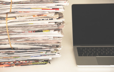 Newspapers and laptop. Pile of daily papers with news next to the computer. Modern gadget and old...