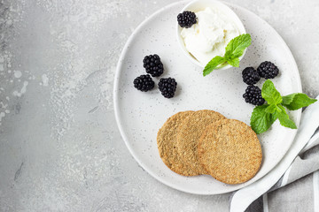 Thin crispy wholegrain crackers with cream cheese, blackberry and mint on a grey plate. 