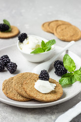Thin crispy wholegrain crackers with cream cheese, blackberry and mint on a grey plate. 