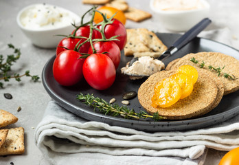 Thin crispy wholegrain crackers with cream cheese and tomatoes on a black plate. 