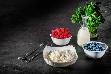 Cottage cheese with fresh raspberries and blueberries in a bowl for healthy breakfast on dark background