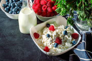 Cottage cheese with fresh raspberries and blueberries in a bowl for healthy breakfast on dark background