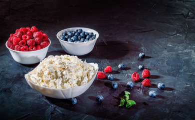 Cottage cheese with fresh raspberries and blueberries in a bowl for healthy breakfast on dark background © Storm