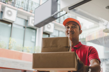 asian young delivery service man in red uniform sending parcel post box to customer at home, cargo shipping, express delivery service, online shopping, service occupation and logistics concept