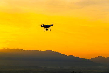 Fototapeta na wymiar Drone quadcopter flying on mountain sunset silhouette scene