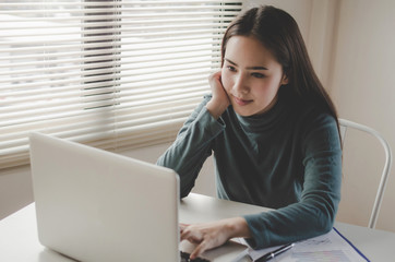 pretty young asian woman typing working and using laptop and document on desk at home office, lifestyle, searching web, social network, online, finance, investment and digital technology concept