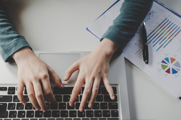 top view hand on keyboard of young woman typing working and using laptop and document on desk at home office, searching web, social network, online, finance, investment and digital technology concept