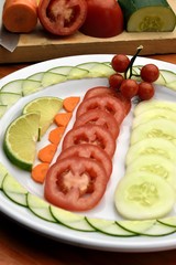 tomato salad, cucumber, carrot, accompanied with a lemon, placed on a white plate on a wooden table and with background the inputs used