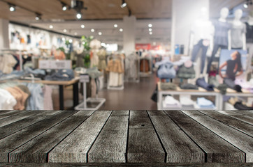 empty grey wooden table or wooden terrace with blurred image of popular fashion clothes shop showcase in shopping mall, copy space for display of product or object presentation, commercial concept