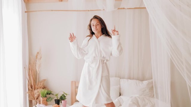 Teenage home leisure. Fun entertainment joy. Energetic girl in bathrobe dancing on bed.