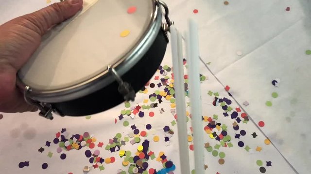 Slow Motion Video Of A Woman's Hand Playing Tambourine, Samba Instrument, Brazilian Carnival. Falling Confetti. White Background. Seen From Above. No People.