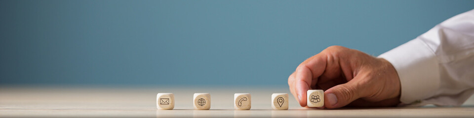 Hand of a businessman placing wooden cubes with contact, communication and location icons