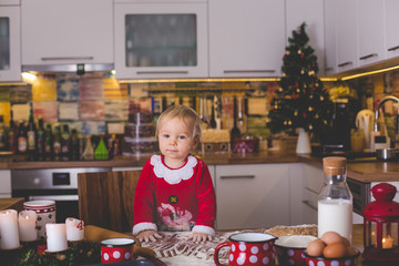 Sweet toddler child, boy, helping mommy preparing Christmas cookies at home