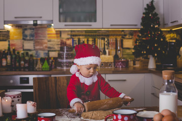 Sweet toddler child, boy, helping mommy preparing Christmas cookies at home