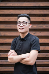 A young korean man in a black t-shirt. Asian man with glasses on a wooden background.