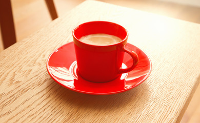 Red cup of coffee on a wooden table.