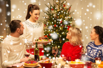 Fototapeta na wymiar holidays and celebration concept - happy friends having christmas dinner at home over snow