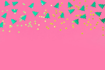 Green metallic foil christmas trees and gold stars confetti sparse on pink background. Simple holiday concept. Design template. Frame with copy space. Winter festive backdrop. Top view, flat lay.